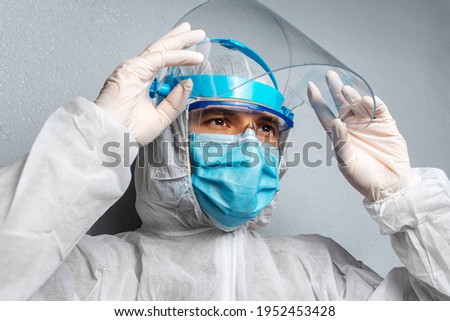 Close-up portrait of a doctor wearing PPE suit against coronavirus and covid-19, on background of grey wall.