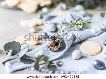 Easter cookies with candies shaped eggs, floral decor and quail eggs on linen napkin, stone background. Holiday concept. Selective focus.