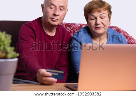Happy elderly couple with a card using laptop on the table at home. High quality photo