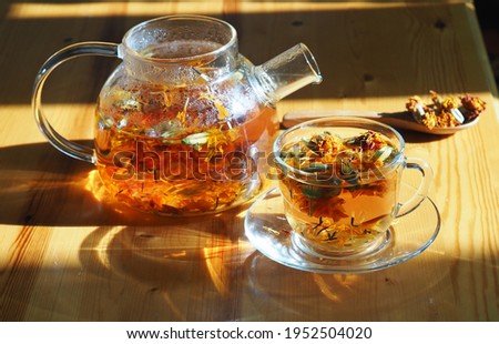 Herbal medicinal tea with dried flowers of marigolds and calendula.Glass teapot with a cup of tea in the evening light.