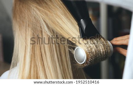 Hair stylist drying client's hair with a brush comb and a hair dryer at beauty salon Royalty-Free Stock Photo #1952510416