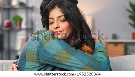 Close up portrait of Hindu happy lovely couple hugging while sitting at home. Side view of caring handsome young husband embracing his beautiful wife feeling grateful, love relations concept