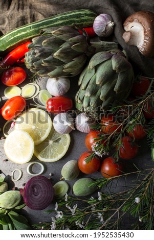 Fresh organic vegetables top view photo. Artichoke, cherry tomatoes, garlic, herbs, onion, zucchini and pepper on a table. Gray background with copy space. Balanced nutrition concept. 