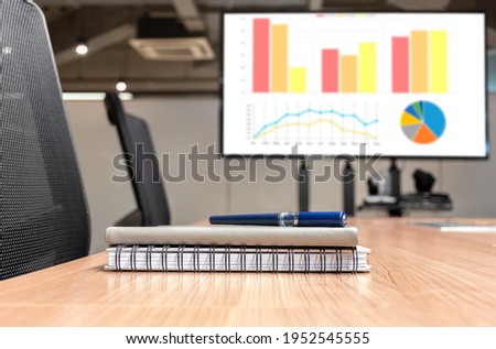 Close up pen and notebook on table with presentation television in meeting room