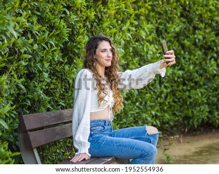 young woman taking a selfie sitting on a bench in the park