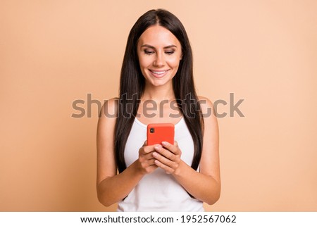Photo portrait of smiling woman holding phone in two hands isolated on pastel beige colored background