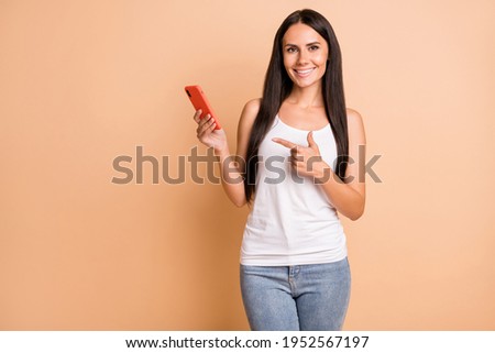 Photo of optimistic brunette girl point telephone wear white top jeans isolated on pastel beige color background