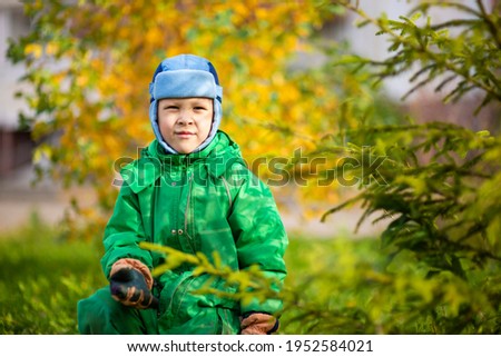 A small child in an autumn suit and a funny hat on the lawn under the open sky is cute stomping and smiling. It's autumn outside, yellow leaves on the trees, a clear sunny day. image with selective