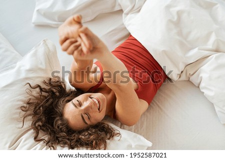 Top view of cheerful woman waking up after sleep and stretching on bed. High angle view of beautiful girl lying on bed and stretching after wake up. Awake woman wake up in morning and feeling fresh. Royalty-Free Stock Photo #1952587021