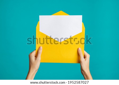 Women hand holding yellow envelope and card. Woman hands holding empty white card and open yellow envelope letter on blue background. Close up of girl showing empty letter ready for your text.