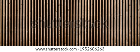 Panorama of a brown slatted partition wall with two rows of small brackets in front of dark background Royalty-Free Stock Photo #1952606263