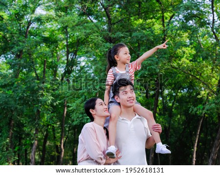 Happy family of three standing in the park pointing 