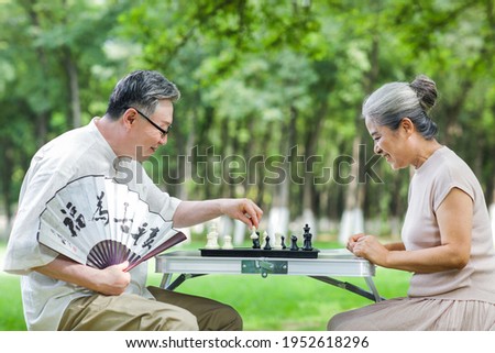 Happy old couple playing chess in the park in summer Royalty-Free Stock Photo #1952618296