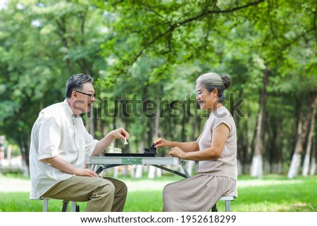 Happy old couple playing chess in the park spend leisure time