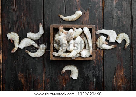 Frozen raw uncooked tiger prawns, shrimps set, on old dark wooden table, top view flat lay
