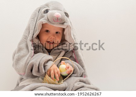 baby in a hare costume holding a basket of Easter eggs.