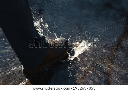Close-up view of men's feet in boots walking along a spring park alley with puddles. A splash of water from the boots