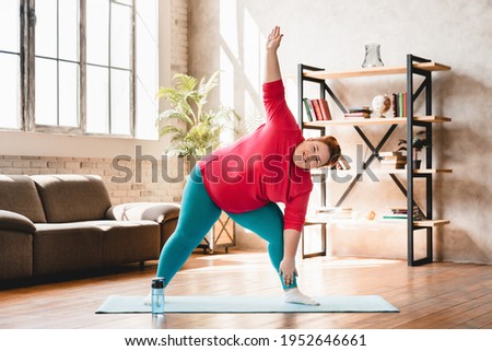 Plus size corpulent young woman doing physical exercises indoors for being in good shape. Dieting and healthy lifestyle for burning fat and calories Royalty-Free Stock Photo #1952646661