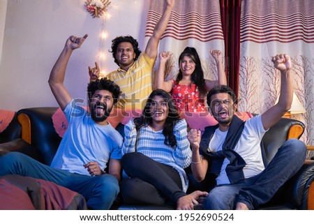 Group of Indian cricket fans shouting and cheering up to support the team while watching sports on tv at home Royalty-Free Stock Photo #1952690524