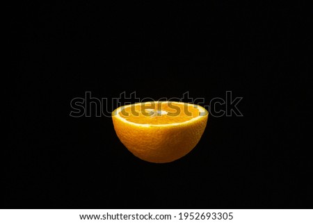 Half an orange on a dark background. Sliced orange on a black background. Creative photography of orange