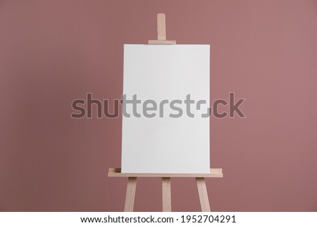 Wooden easel with blank canvas on dusty rose background