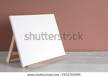 Wooden easel with blank canvas on white table. Space for text