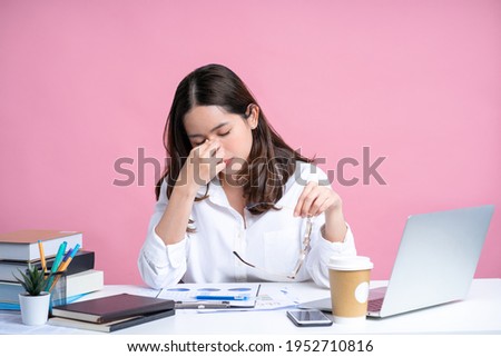 Young Asian woman are stressed and tired from work. She was holding glasses at a white desk with a laptop in the office. Isolated on a pastel pink background. Royalty-Free Stock Photo #1952710816