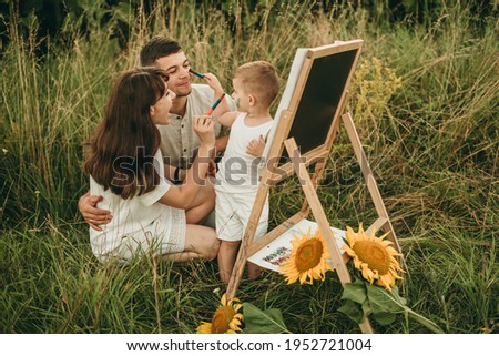 Portrait of a beautiful happy European family paints with a brush a picture on the nature. Development of the child's creativity. Art, parents, childhood, skills, artist. Happy child, drawing lessons.