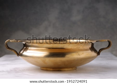 Urule or Brass vessel,an empty traditional  south Indian cooking vessel which is very shiny placed on grey textured background. Royalty-Free Stock Photo #1952724091