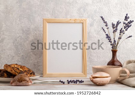 White wooden frame mockup with lavender in ceramic vase, linen textile, cup of coffee and bun on gray concrete background. Blank, vertical orientation, still life.