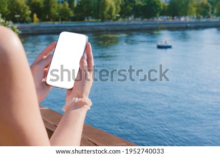Mock up of a frameless smartphone in the hands of a girl from the pier. Against the background of the embankment of the bay