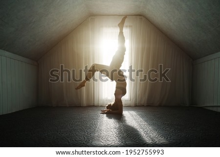 Woman doing morning yoga exercises headstand pose near big window at home