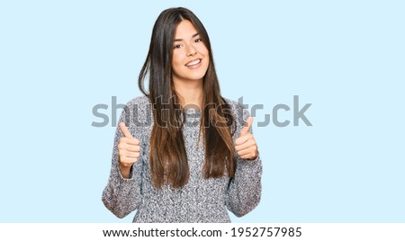 Young brunette woman wearing casual winter sweater success sign doing positive gesture with hand, thumbs up smiling and happy. cheerful expression and winner gesture. 