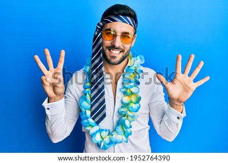 Young hispanic businessman wearing party funny style with tie on head showing and pointing up with fingers number eight while smiling confident and happy. 