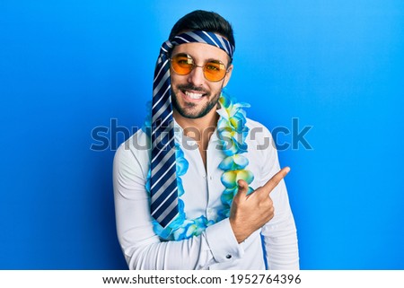 Young hispanic businessman wearing party funny style with tie on head cheerful with a smile of face pointing with hand and finger up to the side with happy and natural expression on face 