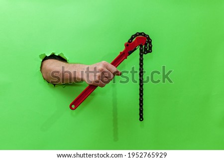 Male hand holds a red pipe key through a torn green paper. Hand through torn green paper. Photo with place for your text, logo and design. Concept repair and tool