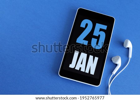 January 25. 25 st day of the month, calendar date. Smartphone and white headphones on a blue background. Place for your text. Winter month, day of the year concept.