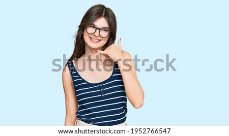 Young beautiful caucasian girl wearing casual clothes and glasses smiling doing phone gesture with hand and fingers like talking on the telephone. communicating concepts. 