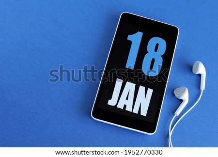 January 18. 18 st day of the month, calendar date. Smartphone and white headphones on a blue background. Place for your text. Winter month, day of the year concept.