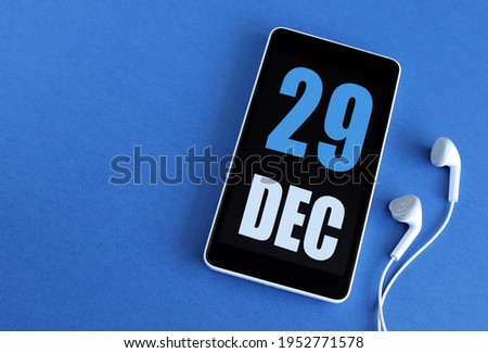 Desember 29. 29 st day of the month, calendar date. Smartphone and white headphones on a blue background. Place for your text. Winter month, day of the year concept.