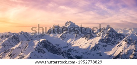 Aerial View from Airplane of Blue Snow Covered Canadian Mountain Landscape in Winter. Colorful Pink Sky Art Render. Tantalus Range near Squamish, North of Vancouver, British Columbia, Canada. Royalty-Free Stock Photo #1952778829