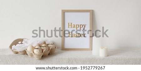 Wooden frame with text "HAPPY EASTER", candles, easter eggs on white background. Easter home decor. 