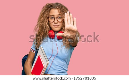 Beautiful caucasian teenager girl holding student backpack and books with open hand doing stop sign with serious and confident expression, defense gesture 