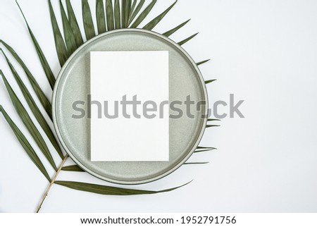 Blank greeting or invitation card mockup with palm leaf and ceramic plate