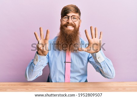 Young irish redhead man wearing business shirt and tie sitting on the table showing and pointing up with fingers number eight while smiling confident and happy. 
