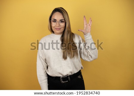 Pretty woman with long hair doing hand symbol against yellow wall