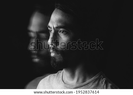 Portrait of a wide-eyed Latino man wearing a beard and a second image of himself with his eyes closed and his face slightly down. Long exposure image. Mental illness concep