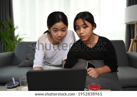 Two asian girl sitting on sofa and watching online cartoons with digital tablet at home.