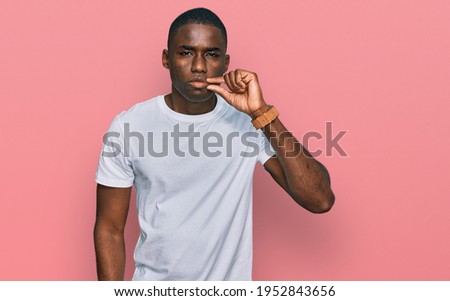 Young african american man wearing casual white t shirt mouth and lips shut as zip with fingers. secret and silent, taboo talking 