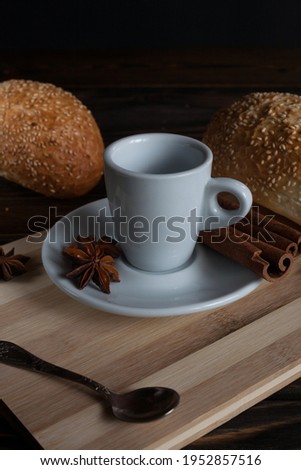 A cup of aromatic black coffee and coffee beans on the table with cinnamon sticks. Morning espresso coffee for breakfast in a beautiful white cup. Against the background of French buns. 